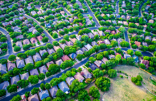 Vast Homes and Thousands of Houses Modern Suburb Development , green boxes of colorful houses below in a curved modern layout and design aerial drone view from high above suburbia