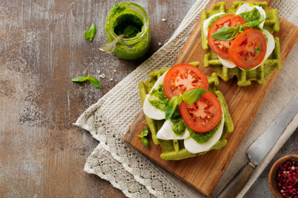 istock Sandwiches on green wafer with spinach and mozzarella cheese, pesto sauce, tomatoes and basil on a gray concrete old background. Selective focus. Top view. 982588708