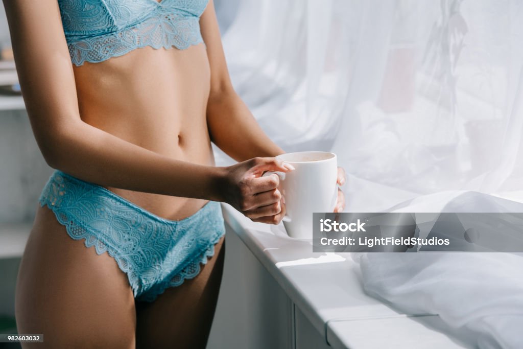 Voir section médiane de slim african american girl en lingerie bleue se tenant près fenêtre avec une tasse de café - Photo de Adulte libre de droits