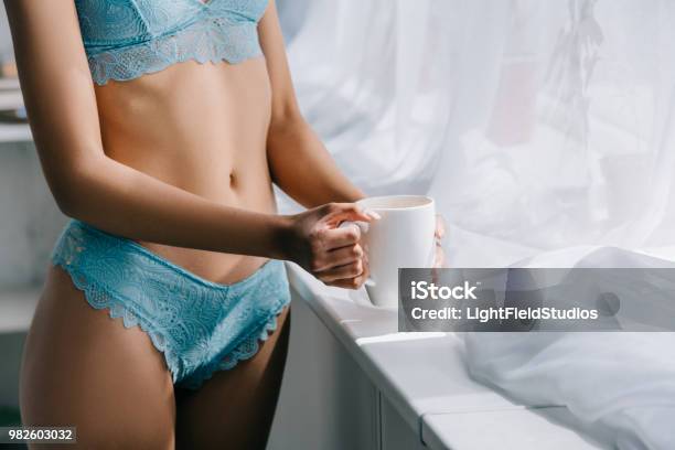 Photo libre de droit de Voir Section Médiane De Slim African American Girl En Lingerie Bleue Se Tenant Près Fenêtre Avec Une Tasse De Café banque d'images et plus d'images libres de droit de Adulte