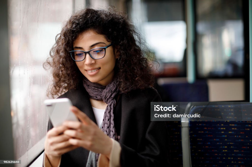 Souriante jeune femme voyageant en bus et en utilisant le téléphone intelligent - Photo de Téléphone mobile libre de droits