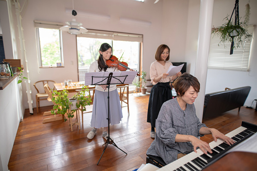 Female friends playing piano, vilolin and singing at home