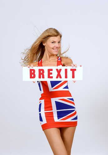 A young woman holds up a large sign with the word Brexit \non it. She stands in front of the camera  and wears a British \nflag dress and demonstrates that she is happier with Brexit.