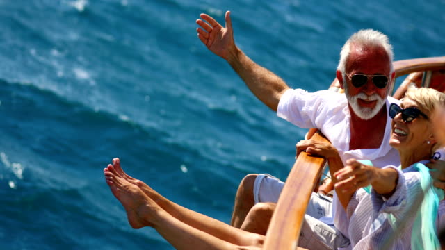 Closeup side view of mid 60's couple enjoying a sailing cruise during  summer vacation at seaside. They are leaning on deck railing and enjoying the view of the sea and horizon. 4k