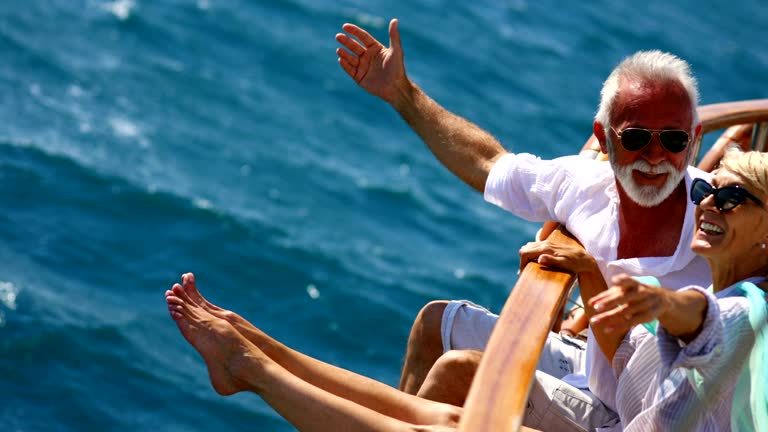 Closeup side view of mid 60's couple enjoying a sailing cruise during summer vacation at seaside. They are leaning on deck railing and enjoying the view of the sea and horizon. 4k