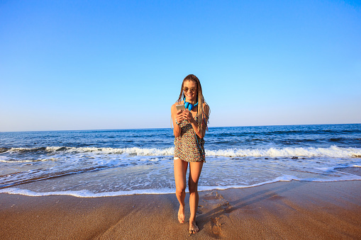 Young woman walking on beach and using smart phone.