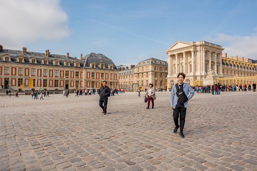 Versailles / France - May 17, 2018: A young tourist poses for a photos while waiting to enter the Palace at Versailles. Millions visit the historic site yearly.