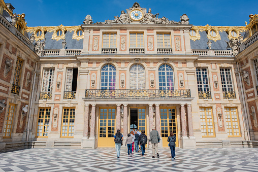 Versailles / France - May 17, 2018: People walking into the entrance of the grand, luxurious Palace of Versailles, on a sunny day. Versailles is a very popular historic tourist site.