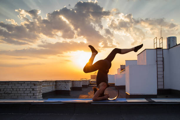 A middle-aged man is engaged in yoga with the use of wheels. A middle-aged man is engaged in yoga with the use of wheels. Yoga on the roof at sunset. shirshasana stock pictures, royalty-free photos & images