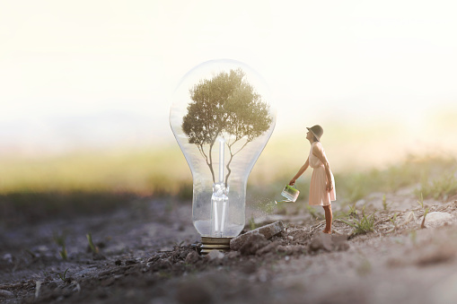 surreal image of a woman watering her plant that needs energy to a light bulb