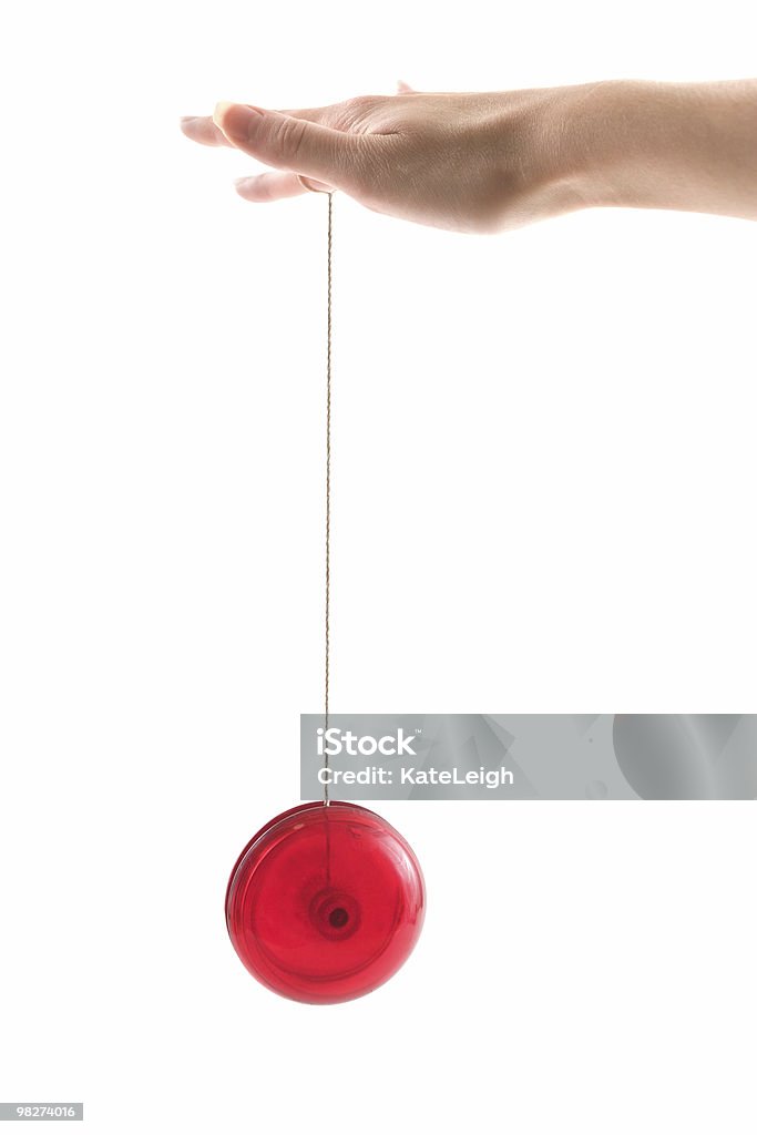 Red yo-yo dangling from a hand on a white background A person's hand playing with a yo-yo Yo-yo Stock Photo