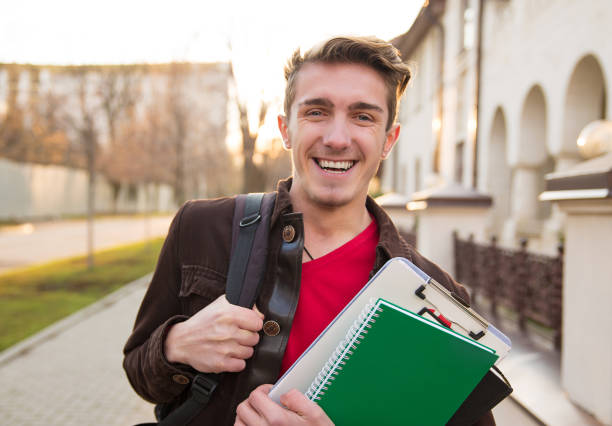 istock Cheerful man with books walking on street 982744830