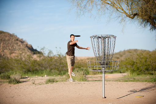 A young man putting during a game of disc golf -  