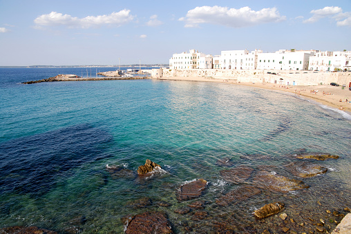 Rocky coast, its caves and the white architecture of its houses at the foot of the Ionian Sea on a sunny summer day.