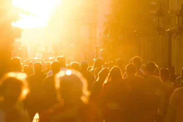 Silhouette crowd of people walking down the pedestrian zone at summer evening sunset, telephoto shot