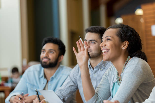 Mid adult woman raises hand duirng college class Confident mid adult college student raises her hand to ask or answer question while attending a college class. indian subcontinent ethnicity stock pictures, royalty-free photos & images