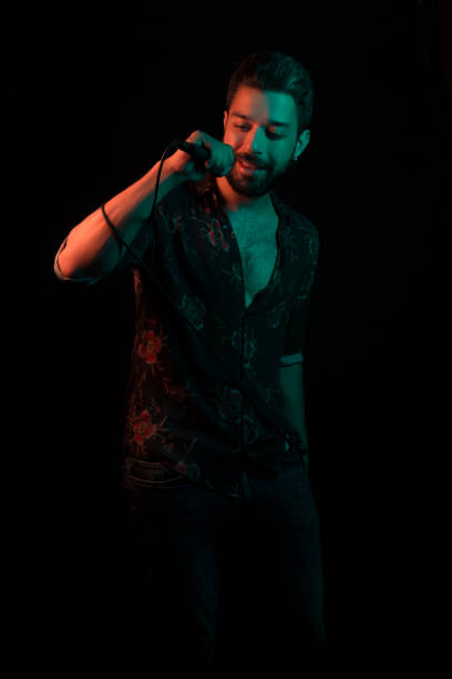 istock Man sings song with microphone on black background with gel lighting/ neon lighting 982811364