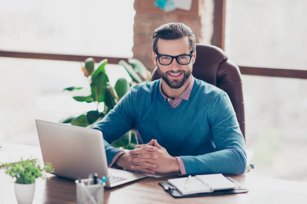 istock Stunning, smiling, harsh, virile, IT-manager in glasses, pullover, shirt, sitting on leather chair at desktop in workplace, looking at camera 982825840