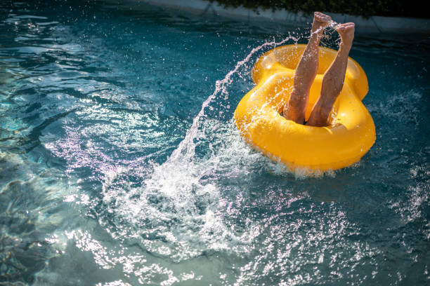 Woman having fun on yellow inflatable ring at water park. She is falling into swimming pool. She is enjoying summer vacation.