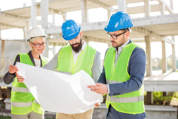 istock Group of architects or business partners discussing floor plans on a construction site 982826890