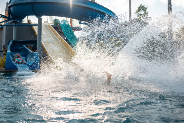 Male friends having fun on parallel water slides. Men are enjoying summer vacation in pool. They are at water park.