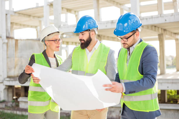 istock Group of architects or business partners discussing floor plans on a construction site 982826926