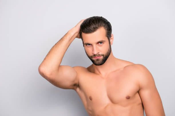 istock Attractive, harsh, virile, flirty, stunning, manly, confident, sportive macho with flawless, smooth, soft skin combing, touching his perfect hair with hand, looking at camera over gray background 982837434