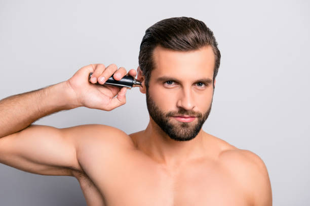 ritratto ravvicinato di un bel maschile muscoloso attraente concentrato uomo concentrato focalizzato usando la holding macchina per rimuovere i capelli dalle orecchie isolate su sfondo grigio - male beauty beauty hairstyle shirtless foto e immagini stock