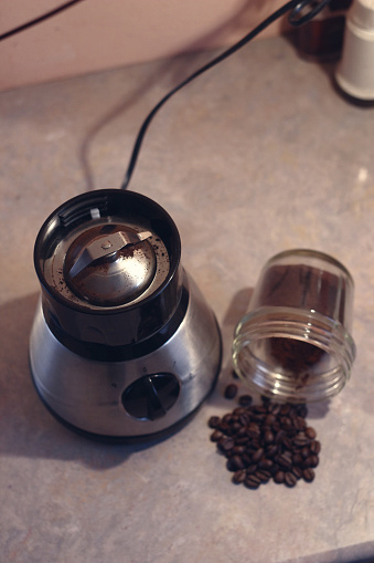 Close up of a grinder with raw coffee beans and in a bowl coffee powder, at home