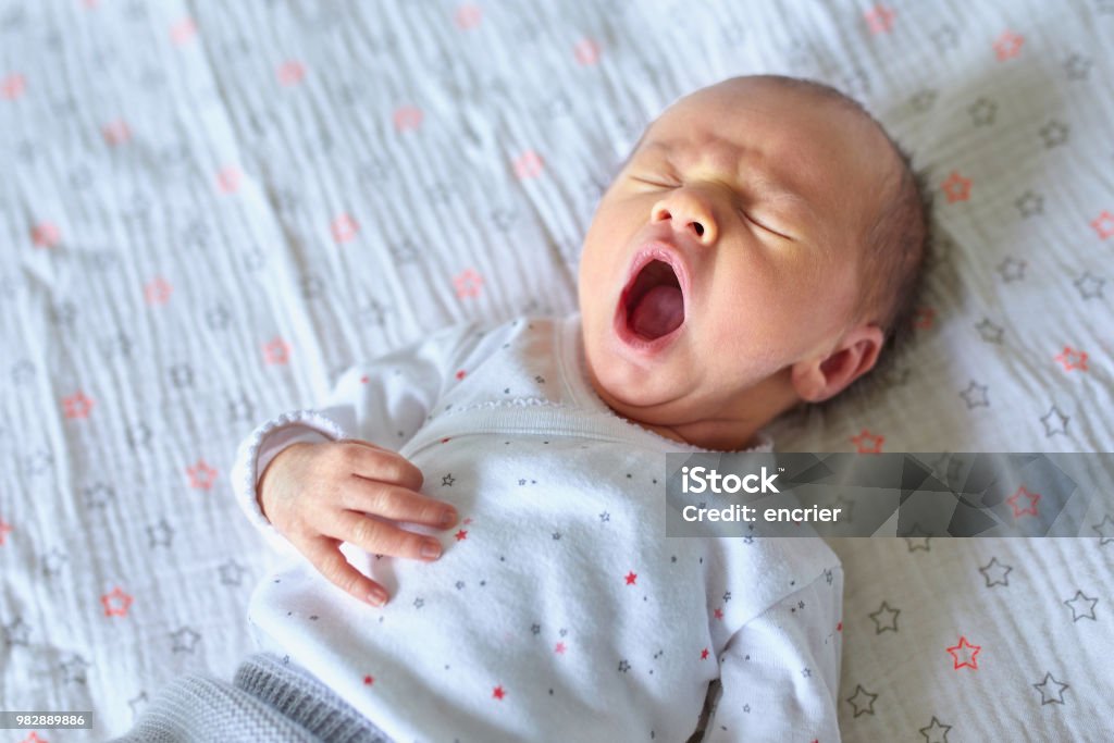 Newborn baby girl yawning Adorable newborn baby girl sleeping and yawning in bed at home Baby - Human Age Stock Photo