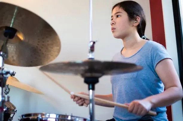 A candid photograph of a 13-year old Eurasian girl playing on a drum kit