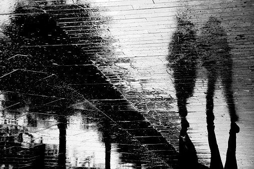 Blurry people shadow silhouette reflection on wet city sidewalk on a rainy day