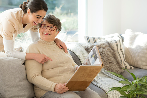 Grandmother sitting on a couch in a sunny room, looking at a photo album and sharing fond memories with a tender caregiver