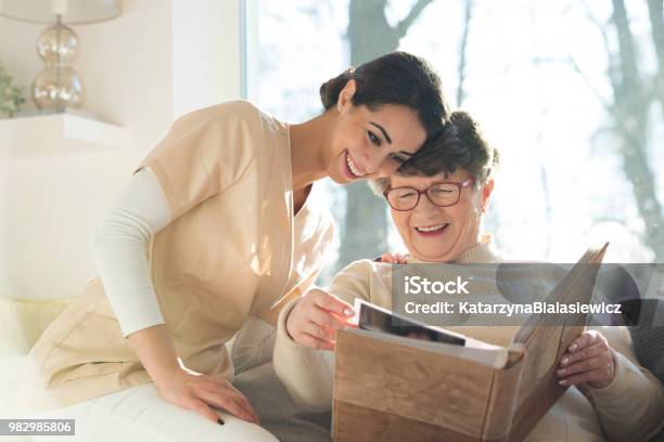 Sonriente Mujer Senior Viendo Álbumes De Fotos Foto de stock y más banco de imágenes de Cuidado - Cuidado, Recuerdos, Residencia para enfermos terminales