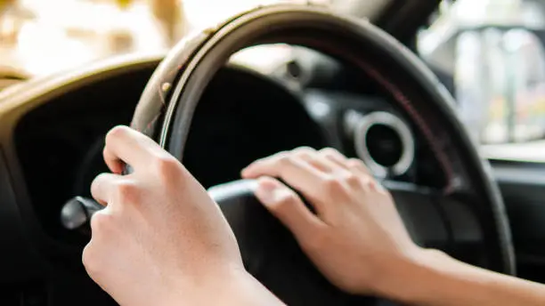 close up of a man hands holding steering wheel while driving right hand drive car on the road.