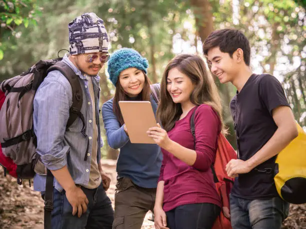 Group of young men/women using tablet for GPS map/planning trekking/traveling in nature forest, backpack traveling for freedom lifestyle with relaxation life outdoor vacation/holiday concept
