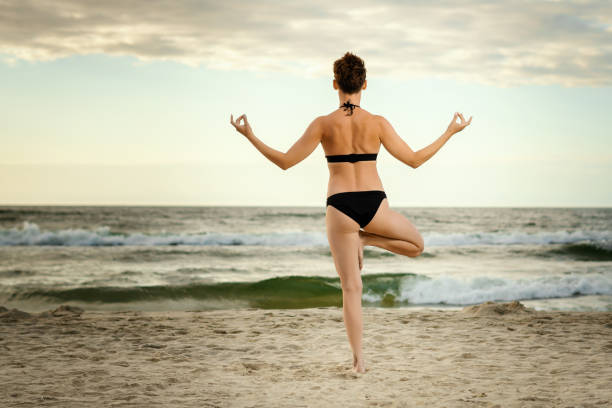 istock beautiful woman practicing yoga on the beach at sunset 983123378