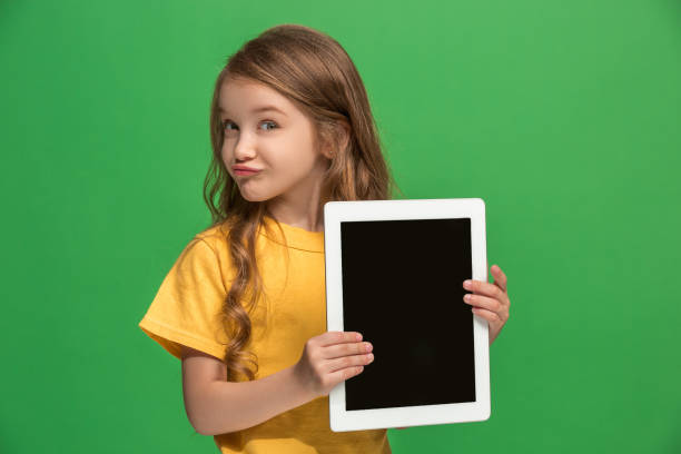 istock Little funny girl with tablet on green background 983138122
