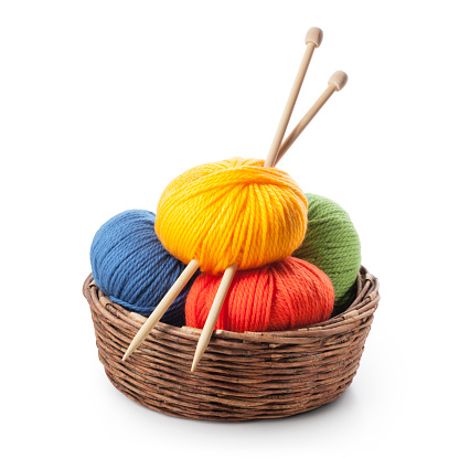 Colored balls of yarn with knitting needles in basket on white background.