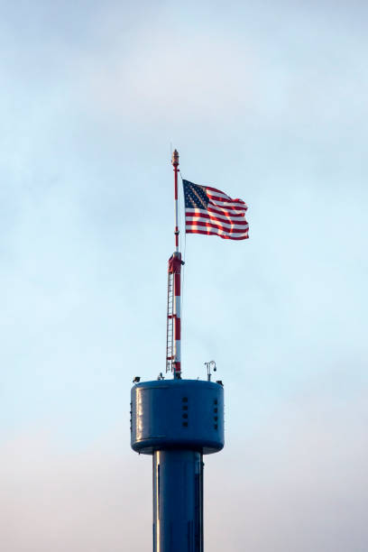 American flag flies over a blue tower with cloud background