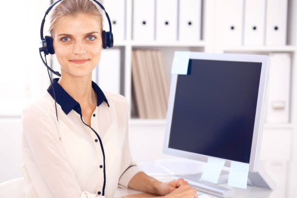 istock Call center operator. Blonde business woman in a headset in white office with pc computer 983187976