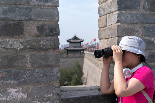 young woman enjoying scenery with telescope on ancient city wall