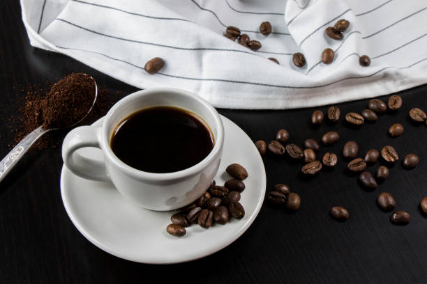 istock Still life with white cup with delicious coffee and coffee beans on dark background 983205020