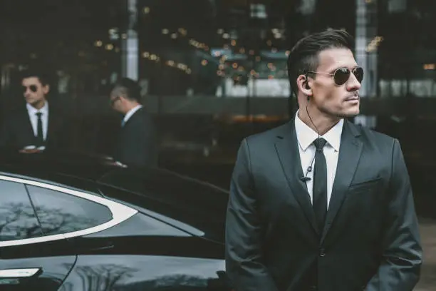 bodyguard standing at businessman car and reviewing territory