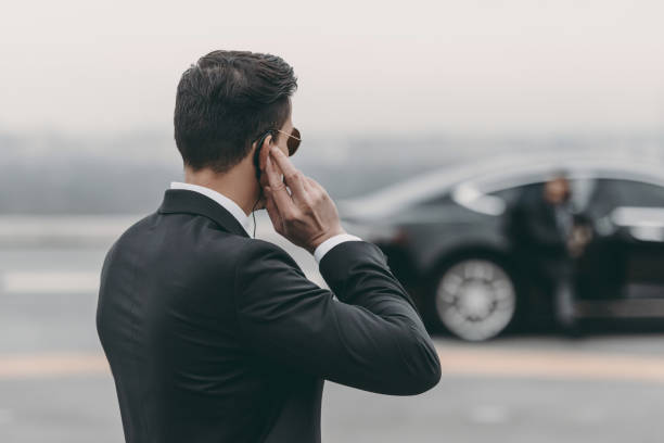 apuesto guardaespaldas de pie y escucha el mensaje con auricular de seguridad en el helipuerto - security guard fotografías e imágenes de stock