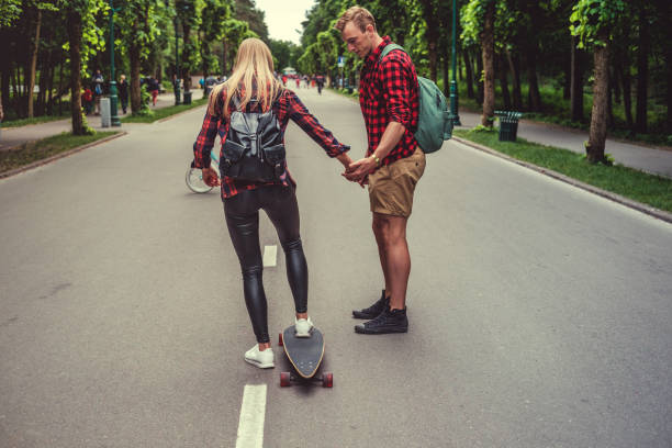istock Blond female learnin ride longboard with casual male. 983243750