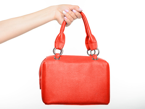 female hand holding red style leather handbag isolated