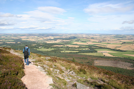 Out of focus shot of a senior man wearing a raincoat hiking uphill in Rothbury, Northumberland. The trail post is in the forefront of the shot.