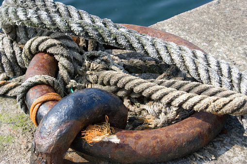 Rusty and weathered ship anchor chain on mooring bollard with sea surface on background