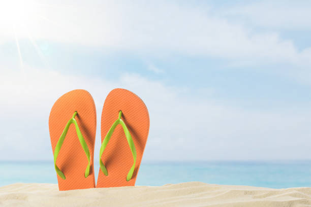 istock Pair of flip flops in sand on blue sky background 983276716